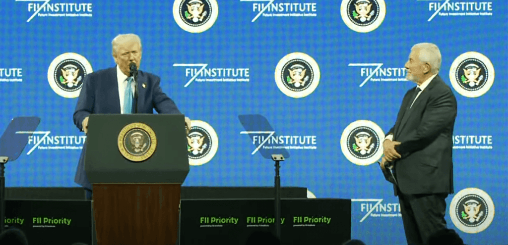 Donald Trump hablando en la Cumbre FII en Miami detrás de un podio con el sello presidencial, acompañado por un líder empresarial en el escenario.